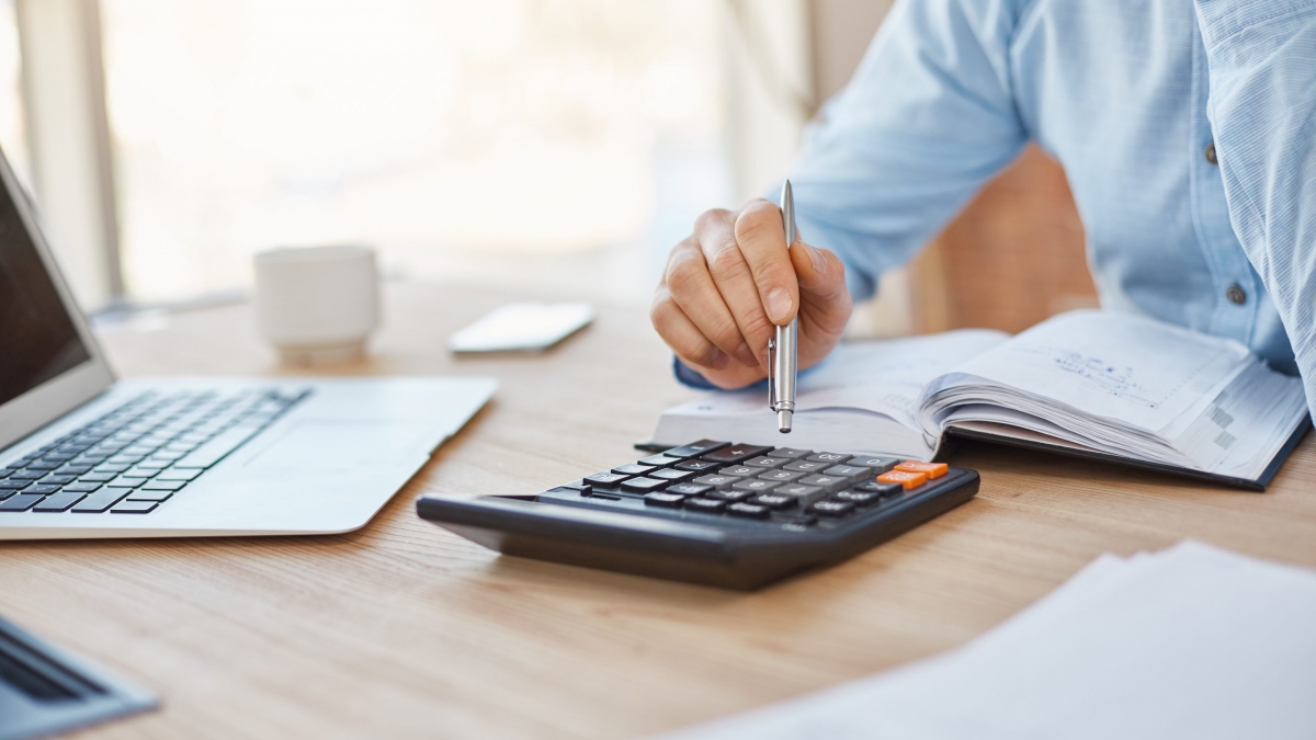 Close up detail of professional serious accountant sitting in light office, checking company finance profits on calculator, writing down results in notebook. Business concept