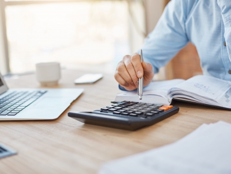 Close up detail of professional serious accountant sitting in light office, checking company finance profits on calculator, writing down results in notebook. Business concept
